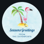 Säsonhälsningar Rosa Flamingo i Santa Hat Runt Klistermärke<br><div class="desc">Stickar med texten: Säsonhälsningar. En viskig teckning av en rosa flamingo som bar en röd tomhatt. Stå på ett berg av strand med gult med grönt och brunt kokosnöt handflatan träd i ryggen. Ljusblå bakgrund med svag polygonal mönster. Tur- och roligt-tropiska former.</div>