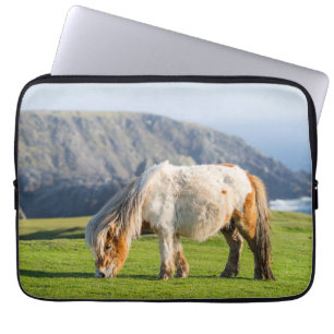 Shetlandponny på betesmark nära höga klippor laptop fodral