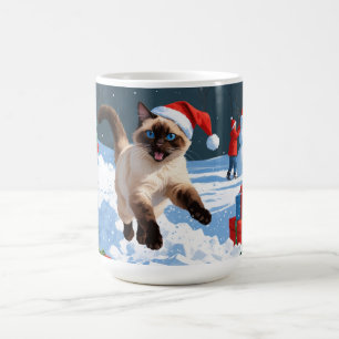 Siamesisk katt springer i snö med julhatt kaffemugg