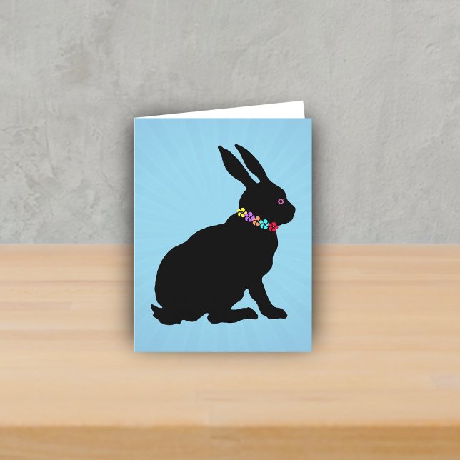 Sidoprofil sittande svart kanin blommor rosa öga kort (Black silhouette sitting rabbit wearing colourful flowers on Spring or Easter blue note card.)