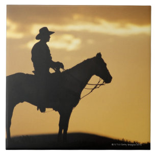 Silhouette av cowboyen på hästrygg på solnedgå kakelplatta