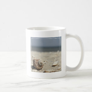 Snäckskal på sanden vid havet kaffemugg