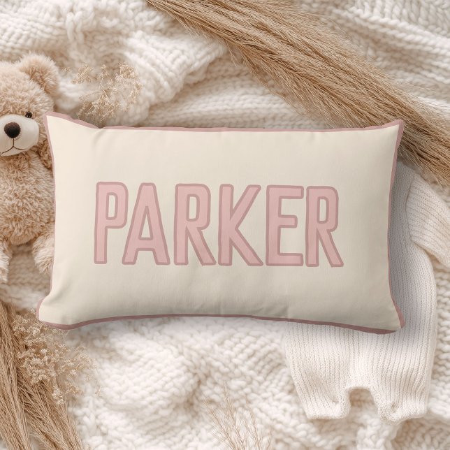 Söt anpassad barnnamn med falsk kant rosa lumbarkudde (A cream pillow with "WILDER" in light pink lettering lies on a cozy, soft-knit blanket)