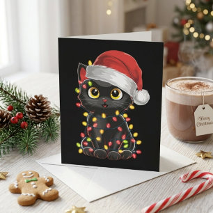 Söt svart katt i tomteluva med julgransbelysning julkort