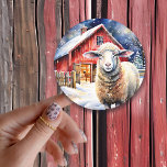 Söt Vattenfärgsfår och Rustic Barn Runt Klistermärke<br><div class="desc">Ett sötfärgsfår som står framför en rustik röd lada på en snögryningsdag.</div>