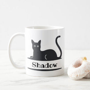 Svart katt som ligger ner med monogram kaffemugg