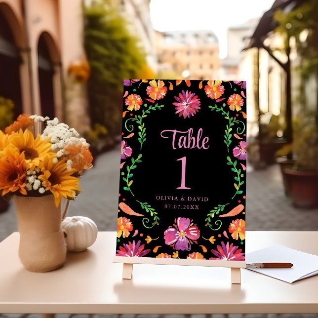 Svart mexikansk blomsterfiesta bröllopsbord nummer (Black Mexican Floral Fiesta Wedding Table Number on a table with flowers.)