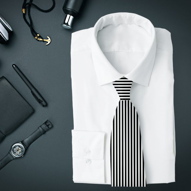Svart och vit tunn lodränd randig slips (A black and white vertical striped tie is featured on an assemblage of men's accessories.)