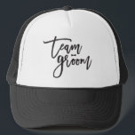 Team Groom Bow Tie Bachelor Party Bröllop Cap Truckerkeps<br><div class="desc">Den här designen har ett modernt och fetstilt svart "teamgroom"-skript för borstad kalligrafi med en snyggt som har en böjningstidsaccent på en klassisk elfenbensvit bakgrund. Bakgrunden färg kan ändras till valfritt färg. Du kan enkelt lägga till mer text/info/information och/eller foton till den här produkten. Fler teckensnitt och redigeringsfunktioner för stilar...</div>