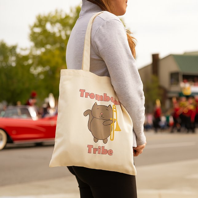 Trombon Tribe Söt Katt Rosa Bokstäver Tygkasse (A tote bag with a brown cat holding a trombone and the words trombone tribe in pink letters.)