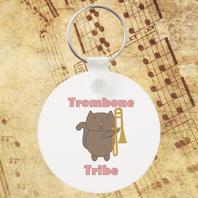 Trombone Tribe Cute Cat Pink Letters Nyckelring (A keychain with a brown cat holding a trombone and the words trombone tribe in pink.)