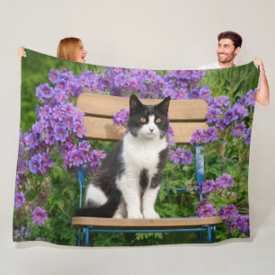 Tuxedo cat sitta på en trädgårdsstol med blommor fleecefilt