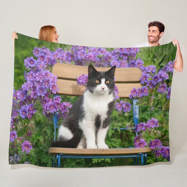Tuxedo cat sitta på en trädgårdsstol med blommor fleecefilt (På plats)