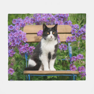 Tuxedo cat sitta på en trädgårdsstol med blommor fleecefilt