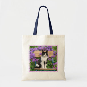 Tuxedo cat sitta på en trädgårdsstol med blommor tygkasse