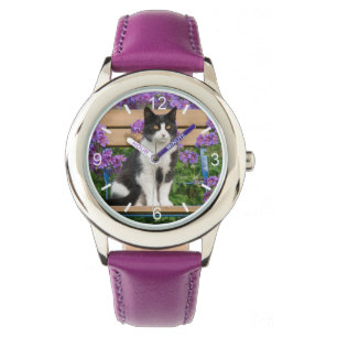 Tuxedo-katt sitta på en trädgårdsstol med blomm armbandsur
