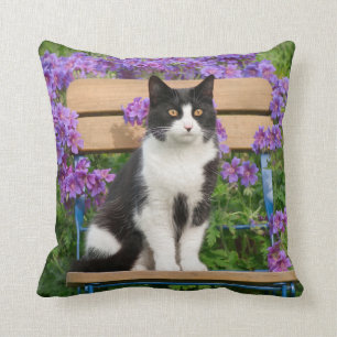 Tuxedo-katt sitta på en trädgårdsstol med blomm kudde