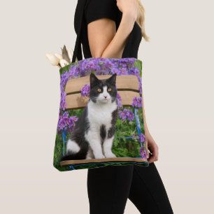Tuxedo-katt sitta på en trädgårdsstol med blomm tygkasse