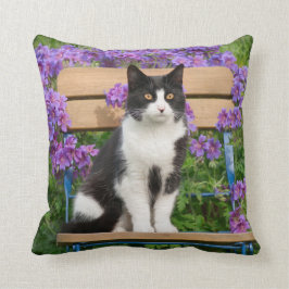 Tuxedo-katt sitta på en trädgårdsstol med blommor kudde