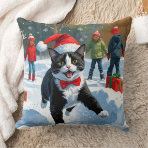 Tuxedokatt springer i snö med julhatt kudde