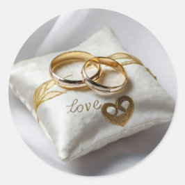 Två bröllop-ringar på en vit kudde runt klistermärke