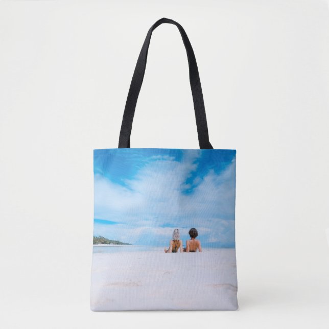 Two women lying on white sand facing beach under b tygkasse (Framsida)