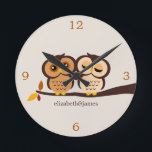 Ugglor i höst rund klocka<br><div class="desc">Den beställnings- märkes- väggen tar tid på särdrag som en förtjusande vektorillustration av en koppla ihop av ugglor perched på en gren i härlig nedgång skuggar av brunt,  orangen och beige. Personifiera med ditt namn,  monogramen,  initialer,  eller en sakkunnig daterar liksom din bröllopsdag!</div>