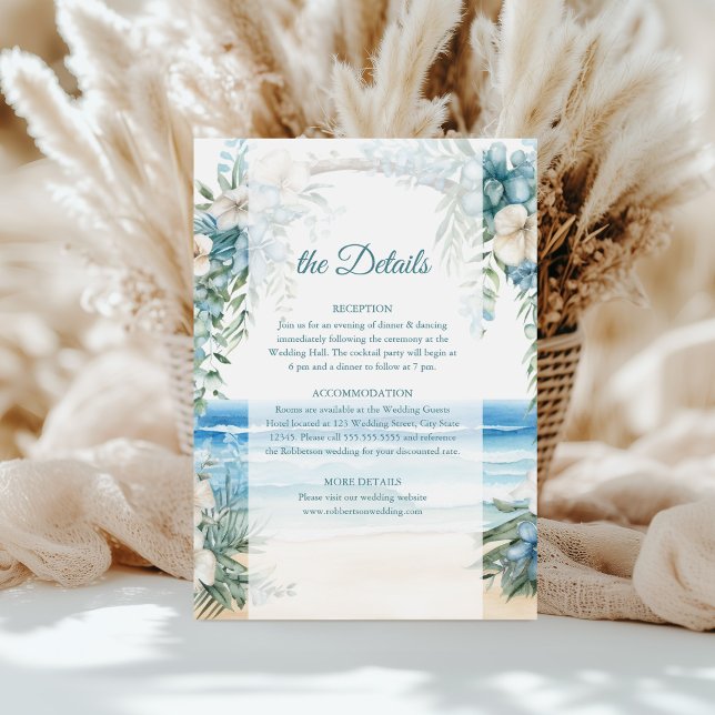 Uppgiftskort för Boho Beach Blue Blommigt Arch Brö Inbjudningar (Boho Beach Blue Floral Arch Wedding Details Card on a table in front of white pampas grass.)