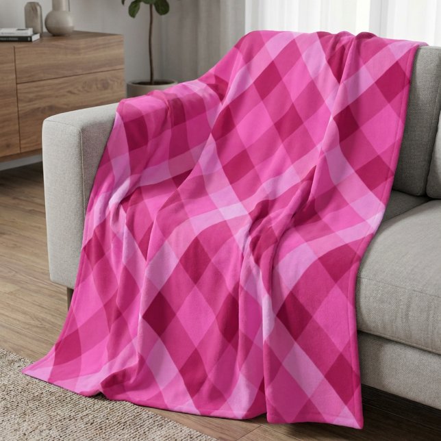 Vacker rosa magenta rutig filt i medium fleece (Beautiful Pink Magenta Plaid Medium Fleece Blanket draped on a sofa in a living room.)