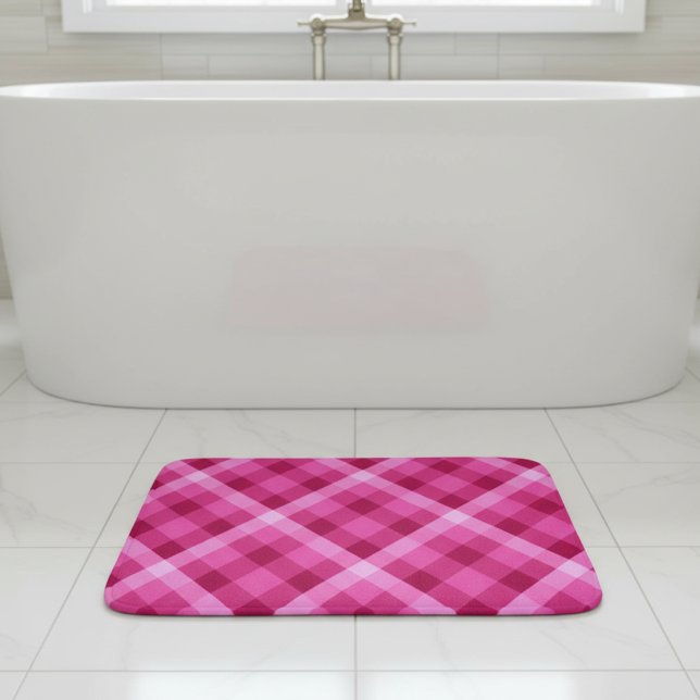 Vacker rosa magenta rutig liten badrumsmatt badrumsmatta (Beautiful Pink Magenta Plaid Small Bath Mat laying flat on tile floor in front of tub in bathroom.)