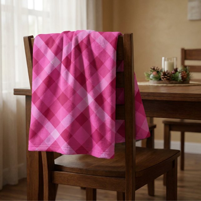 Vacker rosa magenta rutig liten filt i fleece (Beautiful Pink Magenta Plaid Small Fleece Blanket draped on the back of a chair in a dining room.)
