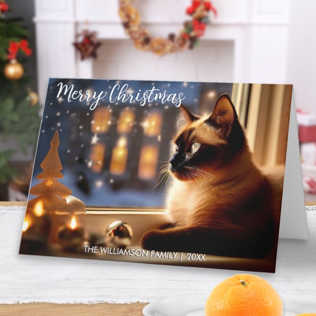 Vackert siamesiskt katt efter fönstersluten jul helgkort (An elegant Christmas card with picture of a Siamese cat looking out of the window at snow and lights)