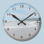 Väggklocka för utfall<br><div class="desc">Tittar du för en strandklocka? Den här klockdesignen kan vara precis vad du är tittar för,  eftersom den har en strandscen där vågar kommer in på en sandstrand och bergen i avstånd. Ett underbart sätt att lägga till ett strandtema till ditt hem. Copyright Kathy Henis</div>