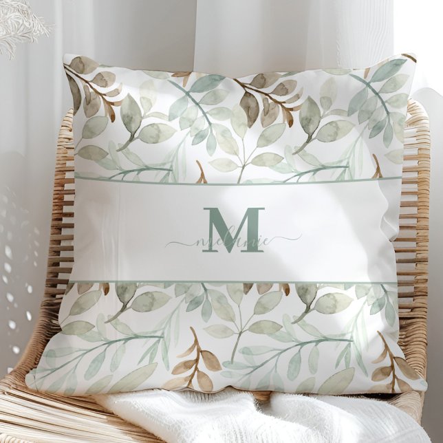 Vattenfärgade löv med eget namn och inledande kudde (Watercolor leaves with Custom Name and Initial Throw Pillow in a sunny rattan armchair.)